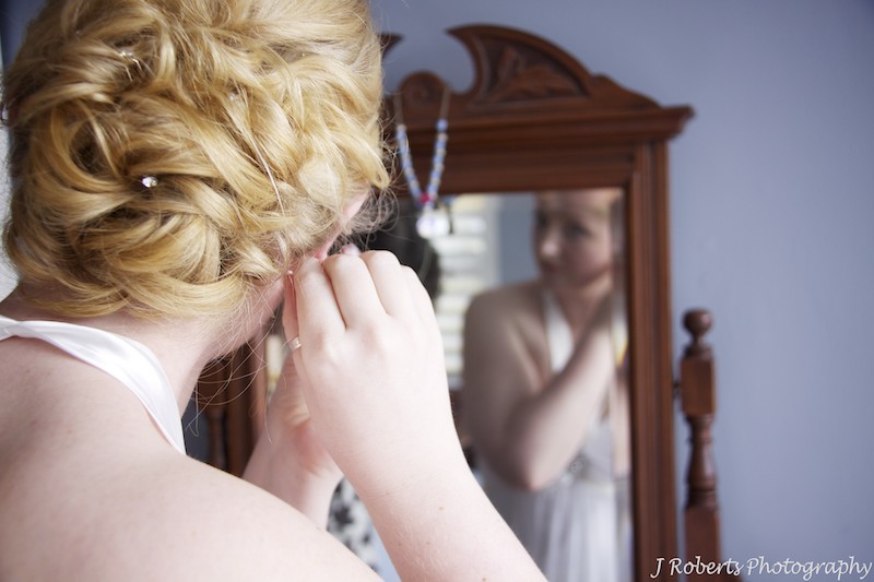 Bride putting earrings in in mirror - wedding photography sydney